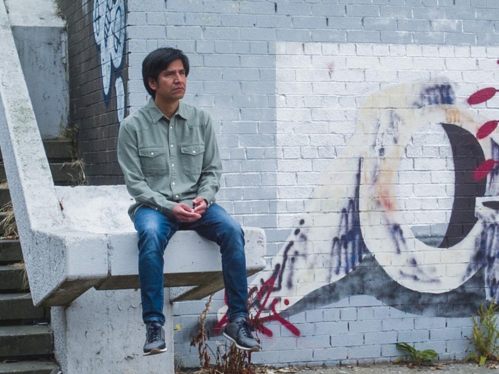 A person sits on a wall next to some steps, there is grafitti on the wall beside them.