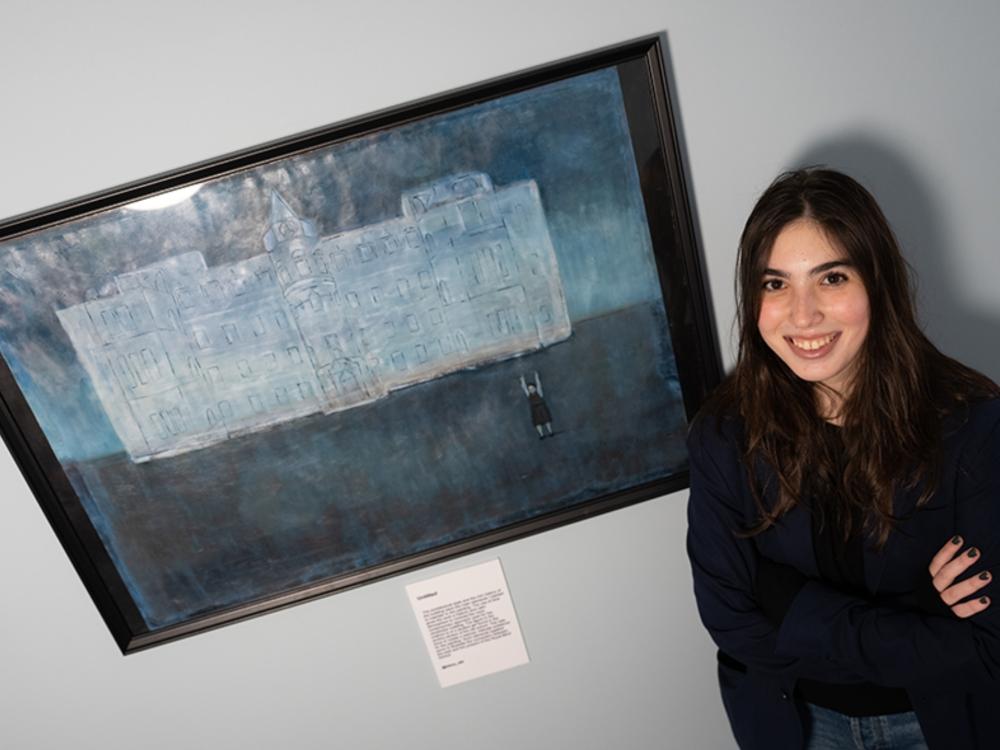 Student standing next to their artwork on the wall.