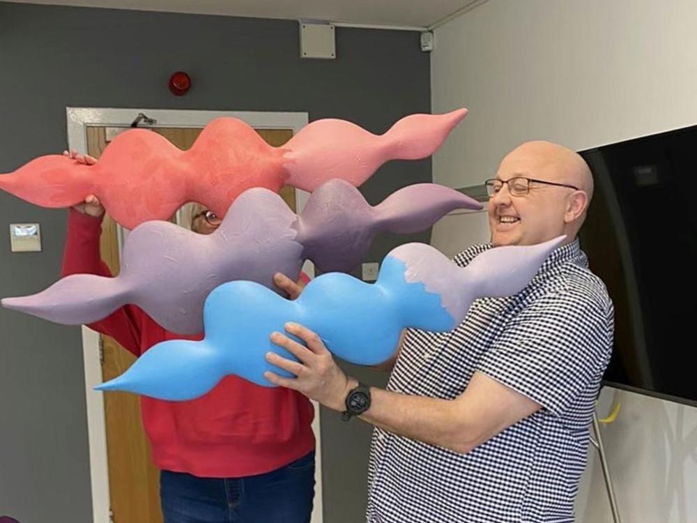 Tommy Whitelaw holds three of the artworks, with another person helping, but hidden behind the artwork.