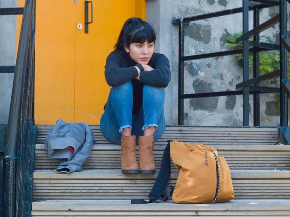 A person sits outside a yellow door on steps, they are leaning on their knees.