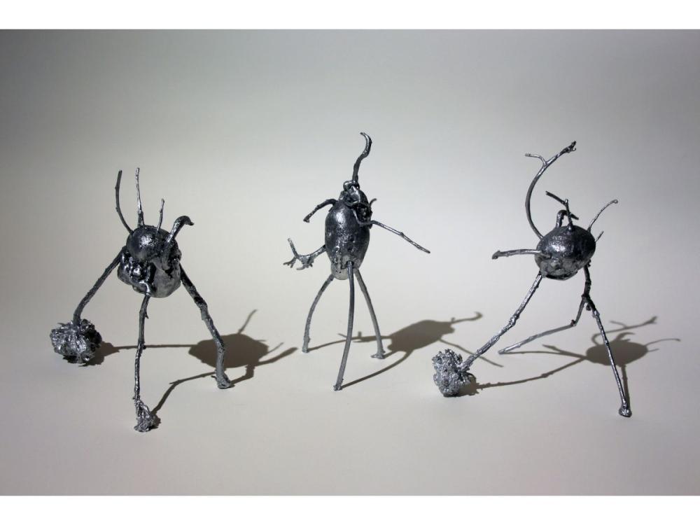 Three abstract metal sculptures - at the centre of each is a shape like a potato, with long, twisting tendrils reaching off. Three of each of the tendrils point downwards, giving each sculpture a tripod-like feel