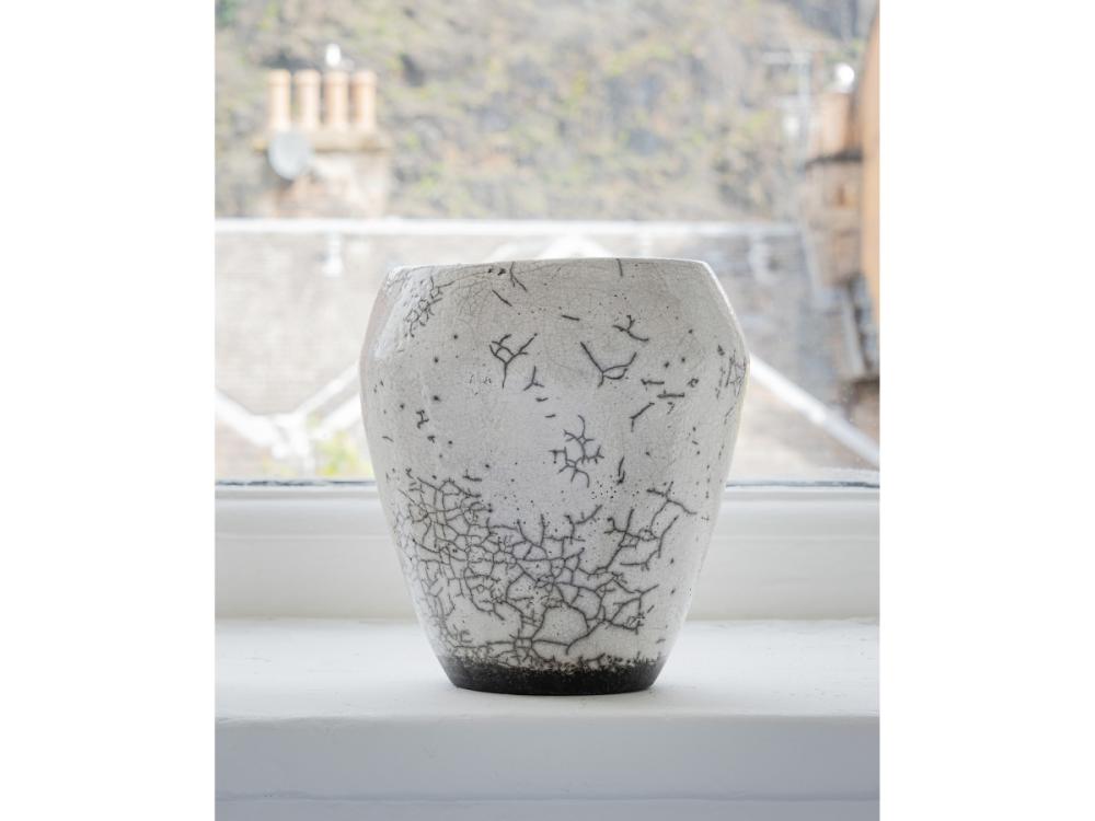 A white pot, wider at the top at the bottom. There's a grey crackle pattern, intense around the bottom and fading up towards the top.