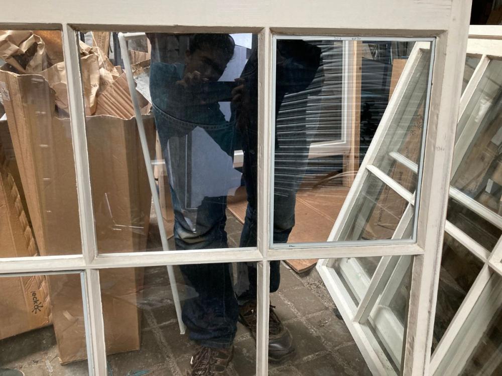 Part of a sash and case window, removed from the building and propped up on the floor. The wider outer frame can be seen, along with the narrower astragals dividing the individual panes.