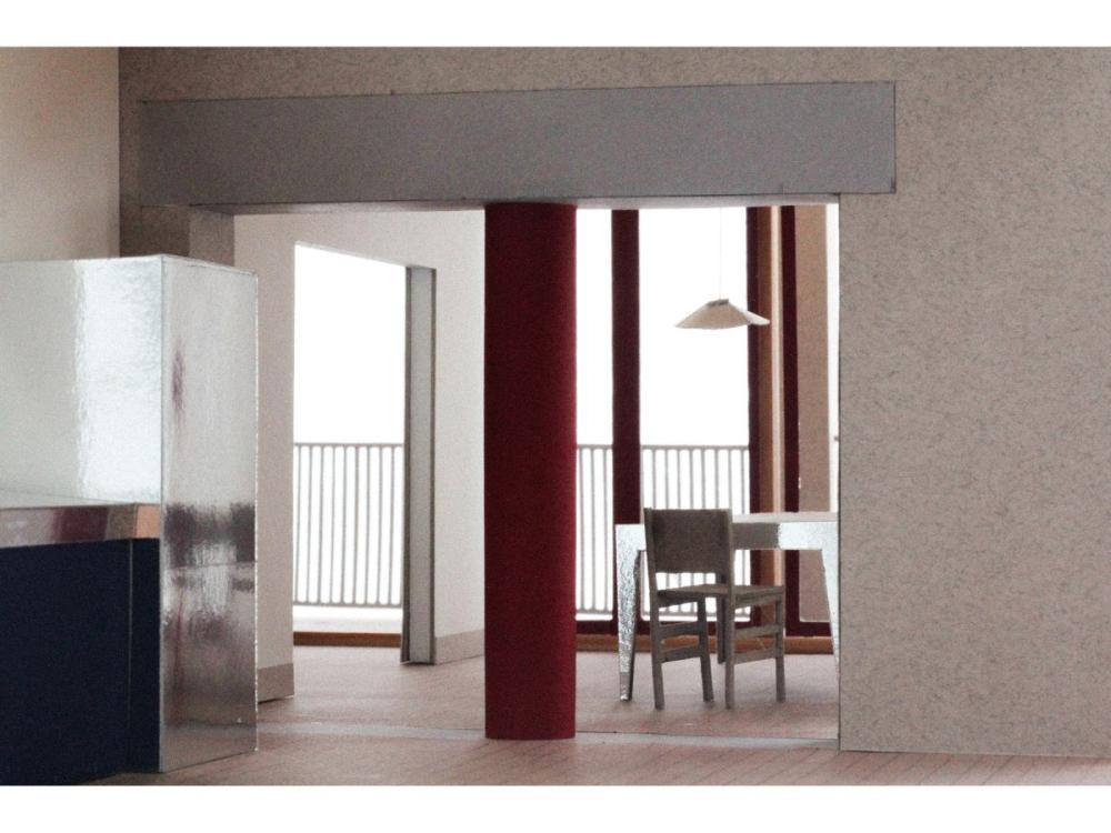 An image of a proposed interior, looking through a wide open doorway with a pillar in the centre, towards a chair and table, with full-height windows behind.