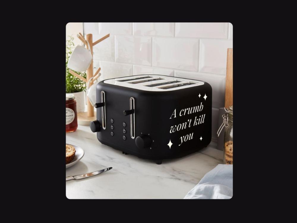 A four-slot black toaster, on a white marble counter. White lettering on the side reads 'A crumb won't kill you'