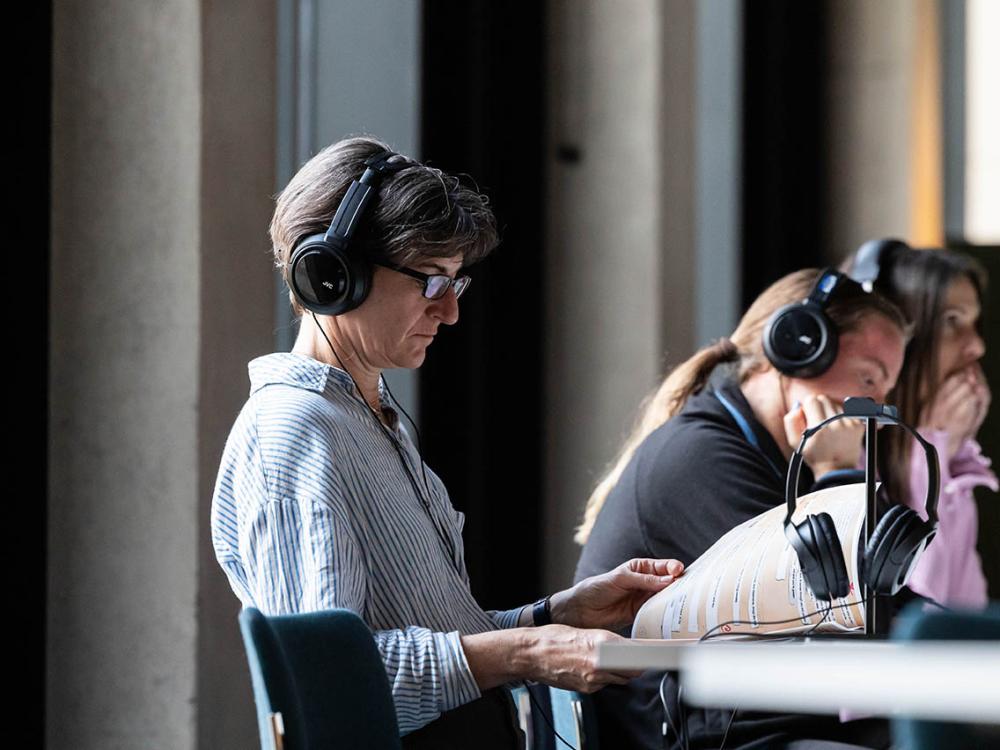 A person wearing headphones is looking at the printed script while listening to the Surface Echoes script. Other people are doing the same.