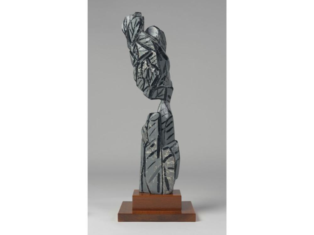 An abstract sculpture comprising grey, angular shapes reaching up from a wooden plinth