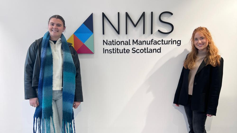 Two students stand next to the National Manufacturing Institute Scotland logo.