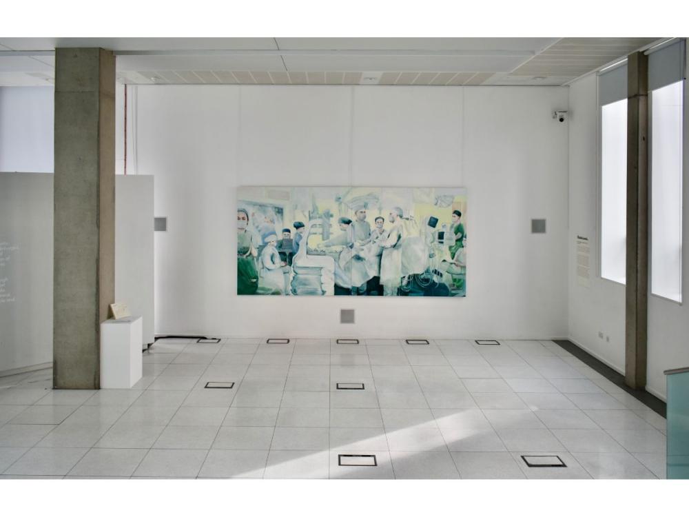 A painting of medical staff at work in an operating theatre, hanging on a white wall in a studio