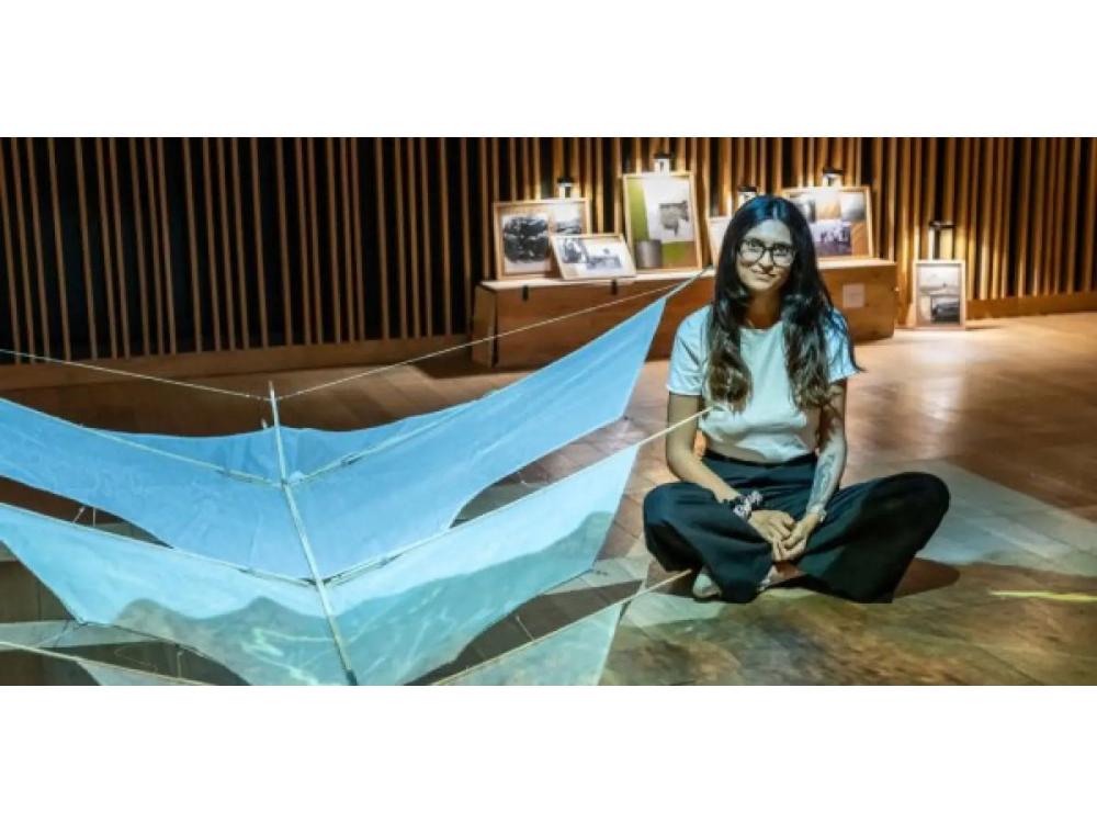 Artist sitting on floor next to exhibit of a kite