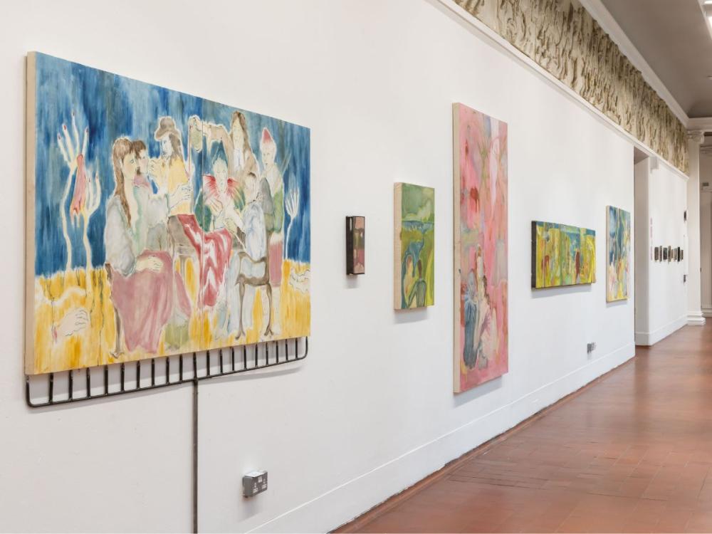 Colourful paintings hung on a white wall. The nearest is of a group of musicians  playing.