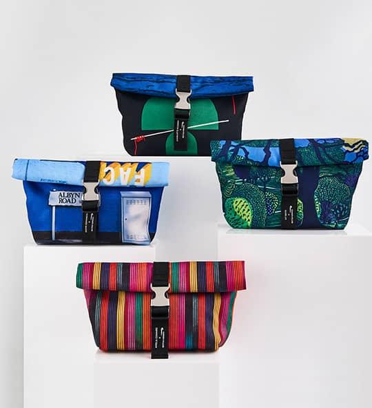 A set of four colourful wash bags are arranged on display plinths against a white background.