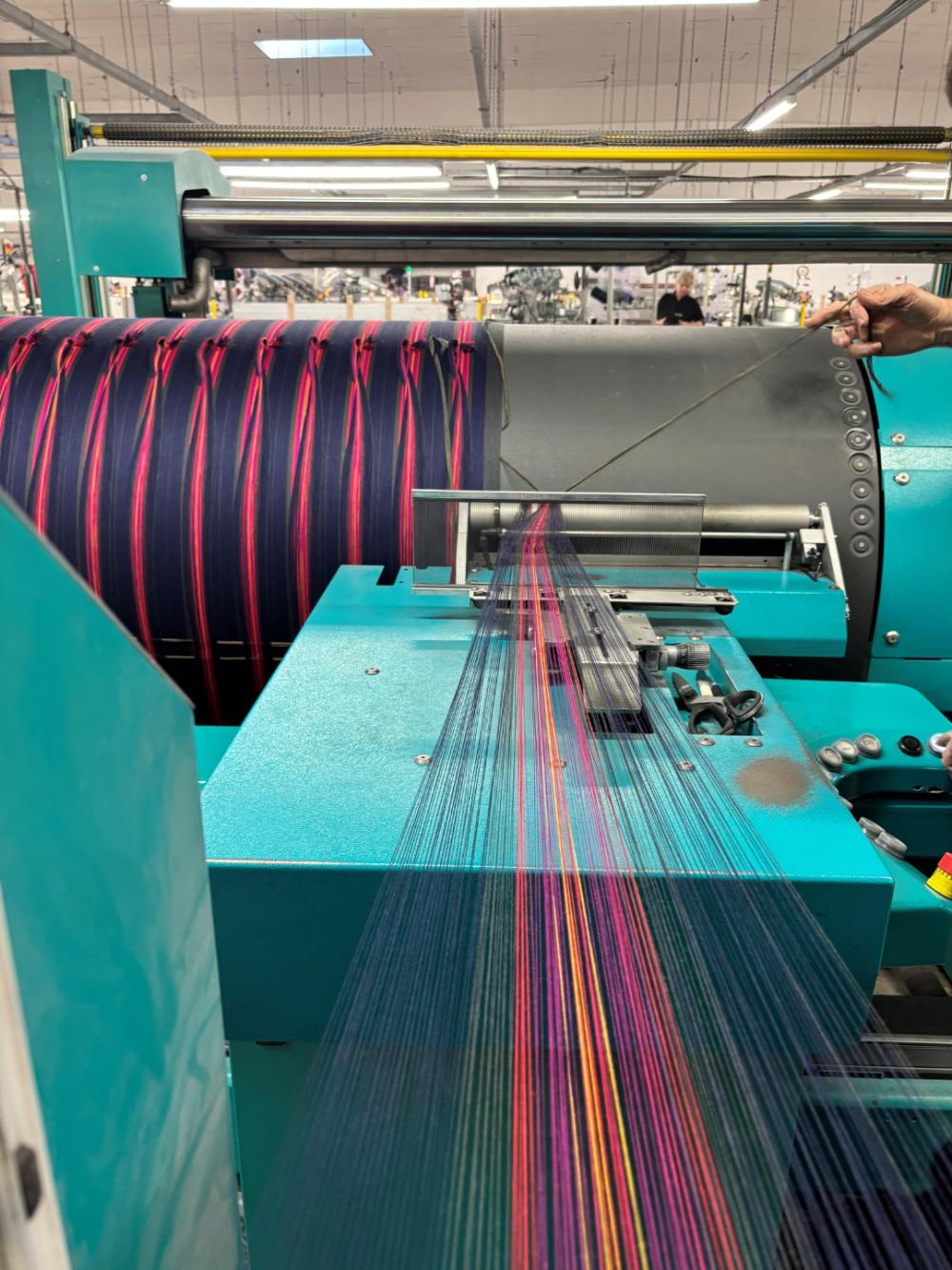 The tartan being woven - long coloured threads stretch towards the loom.