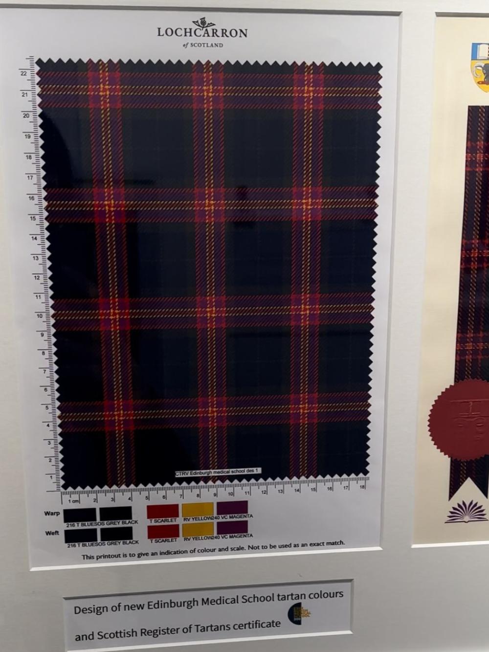 A sample of the tartan on a white board with skeins of thread beneath it.