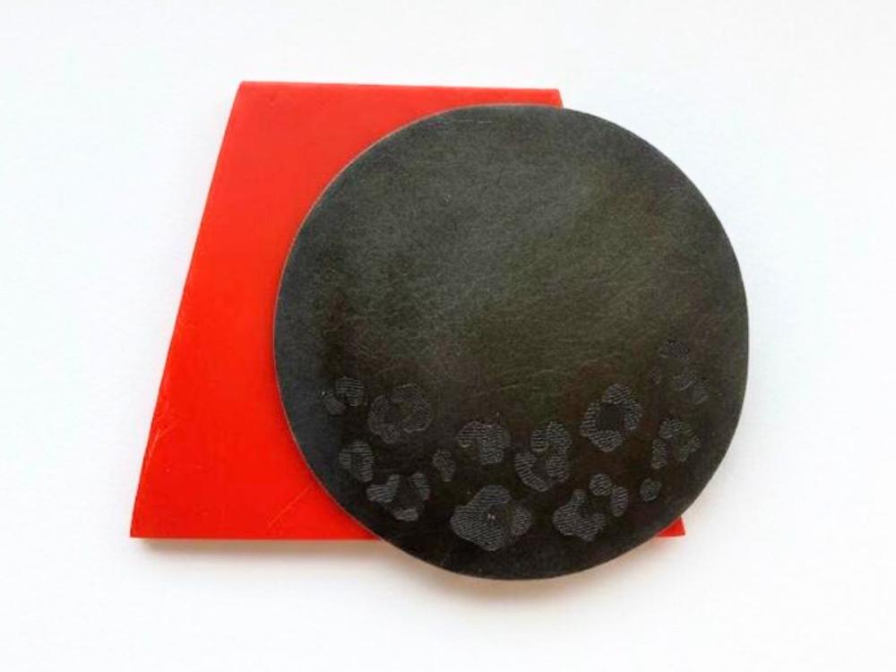 The award, comprising a dark-coloured circle of metal with leopard print on the bottom part, and behind it a red-coloured trapezoid.