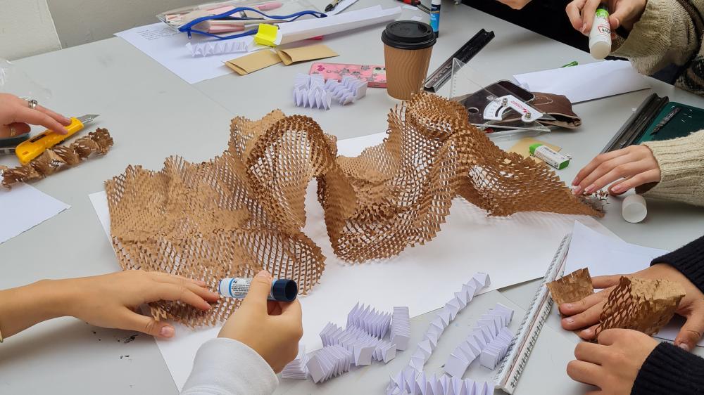 a close up of a table with students working together on materials such as honeycomb packing paper and card.
