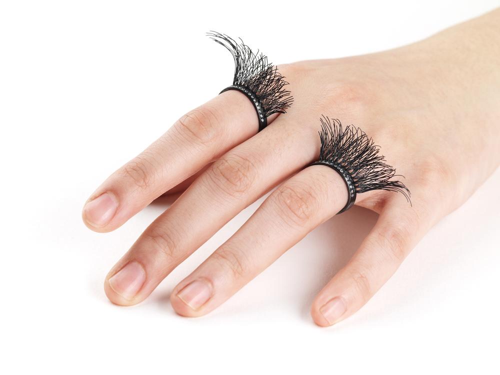 A cheeky hand wears two rings, both formed to appear at first glance to be false eyelashes. 