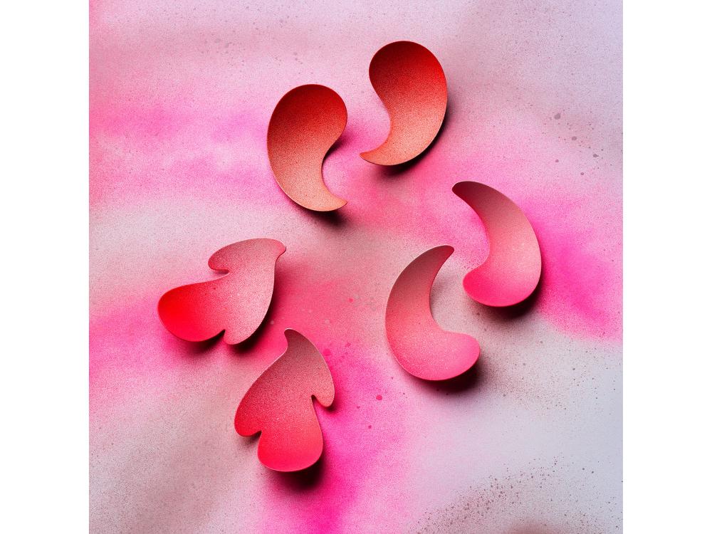 Colourful pink and red earrings sit on a speckled pink background. They are formed of joyful curves and exuberant bright colours. 