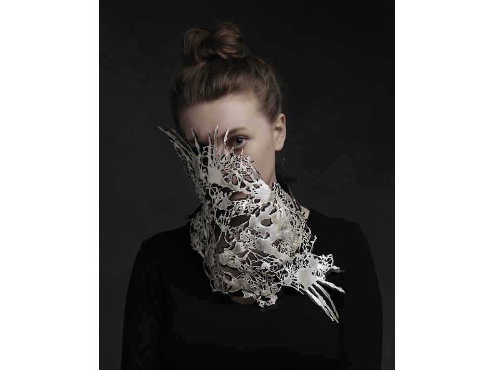 A large silver body sculpture reaches around the neck and up across the face of a model. 