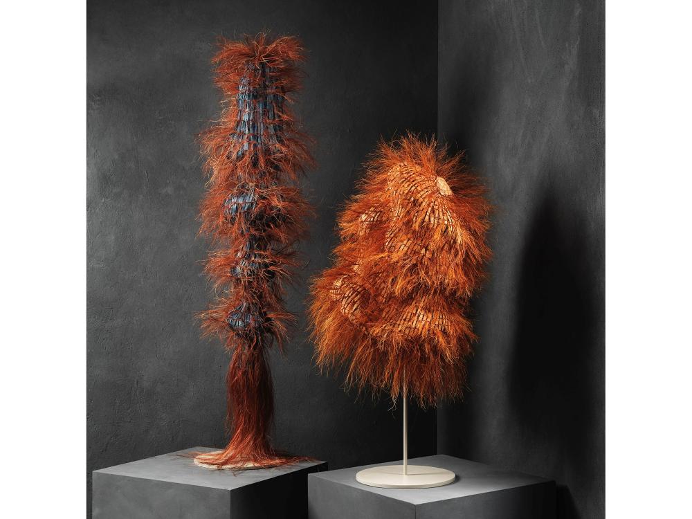 Two bulbous sculptural objects rest on plinths. They are made of woven paper in blues and rich burnt orange tones.  Sisal fibres create a hairy appearance. One is tall and undulating, the other is more squat. 