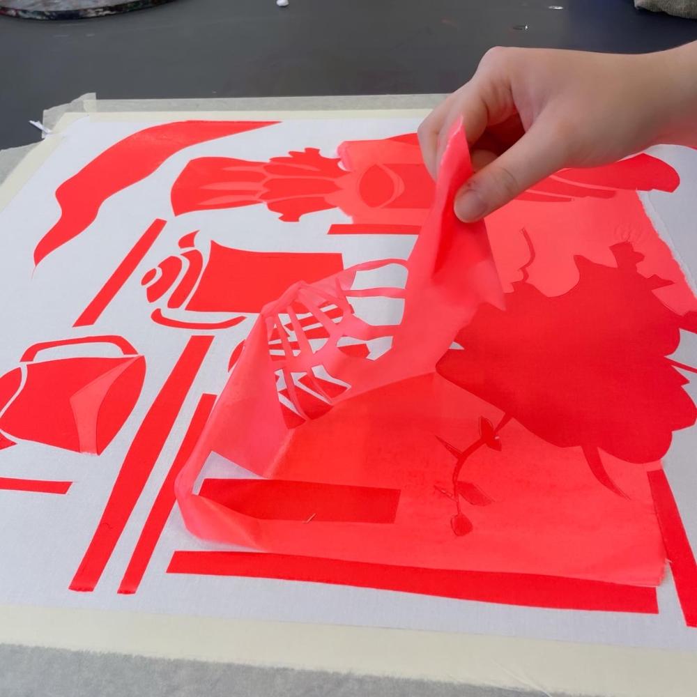 A hand working with bright orange or red fabric on a white background