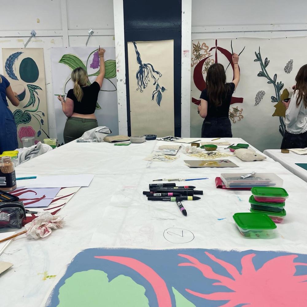 Students painting canvases hanging on a wall in front of them in an art studio