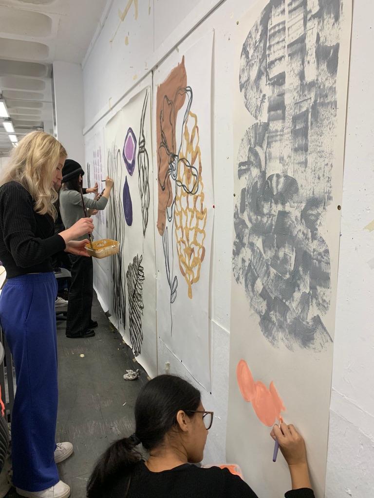 Students painting fabric canvases hanging on a wall in front of them