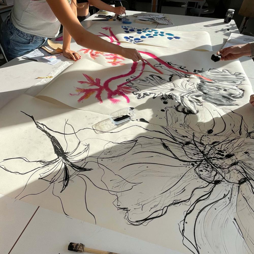 Multiple students working together on painting large floral images on paper on a table