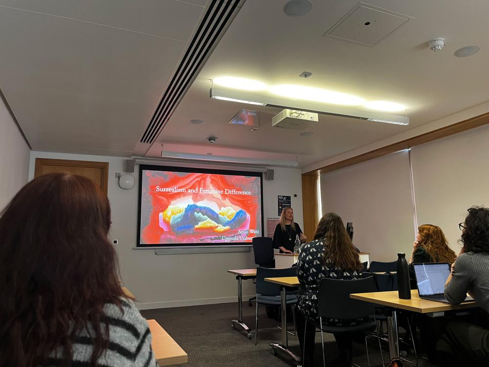 Dr Anna Watz from Uppsala University stands in front of a projector screen, delivering a lecture titled Surrealism and Feminine Difference