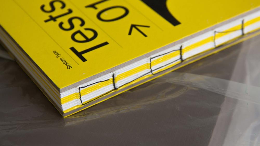 A close up of the edge of a bound yellow book with the word Tests on the front. The pages are striped yellow and white.