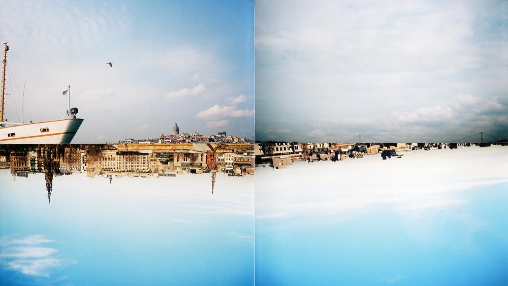 Four film photographs of mostly blue skies, with city landscapes and a boat making up part of the photographs. The two photographs on the lower half of the image are upside down.