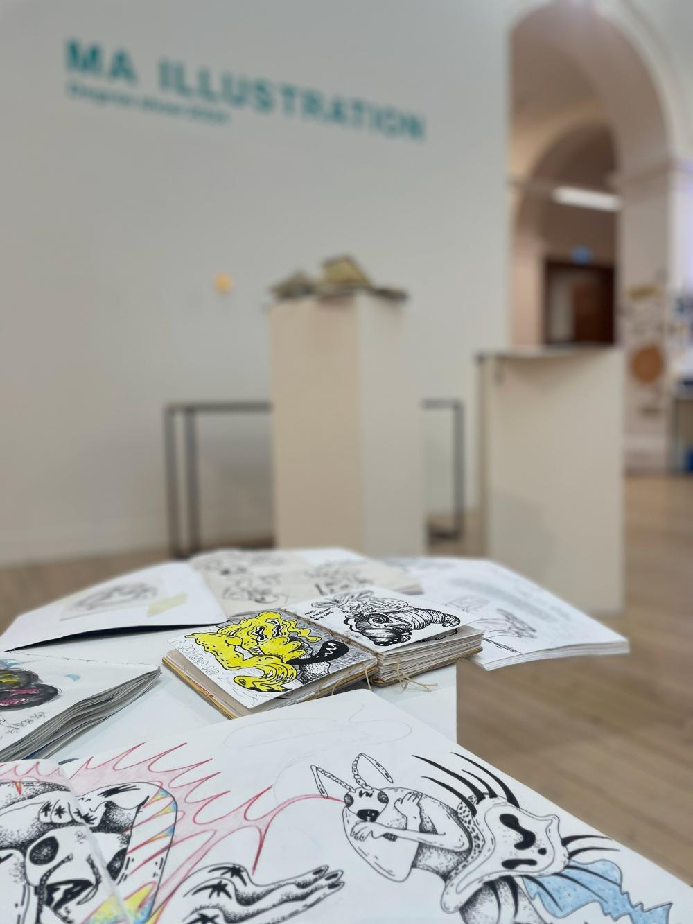 A photograph of an art exhibition, with a close up of an illustrator's sketch books showing their colourful and dynamic drawings.