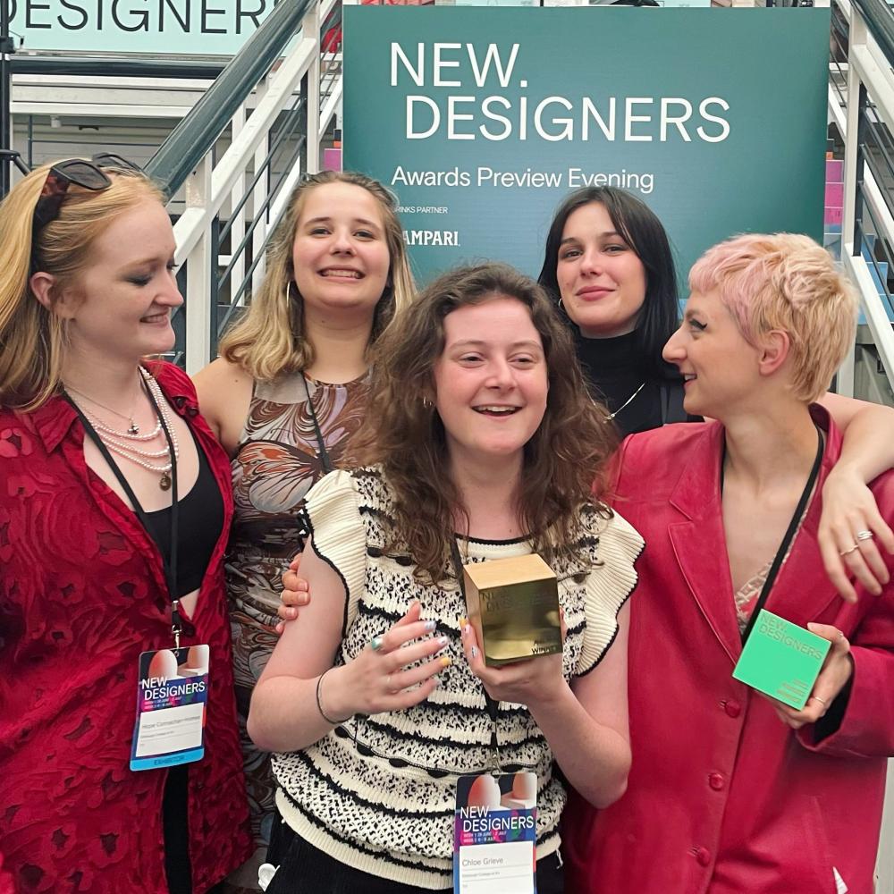 Five women smiling for a photo at the New Designers Event in London. The person in the middle is holding an award.