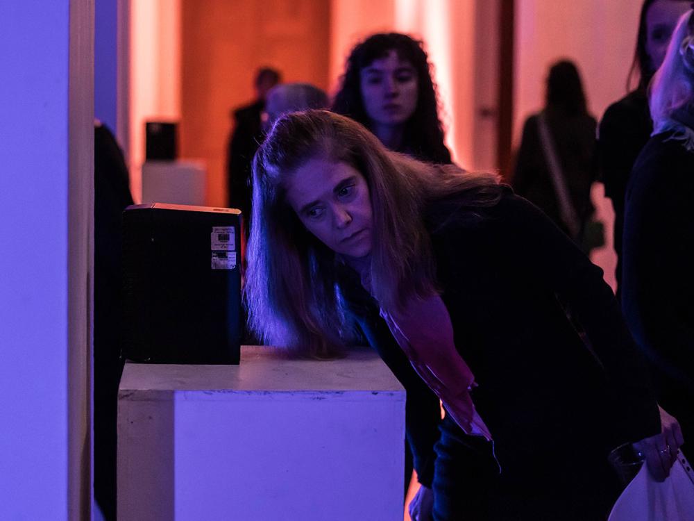 A listener leans in towards a loudspeaker on a pedestal, listening intently.