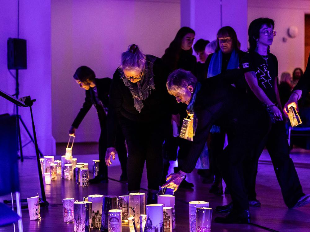 Several people lean down to place glowing lanterns on the floor of the Sculpture Court. The lanterns are decorated with images of Edinburgh.