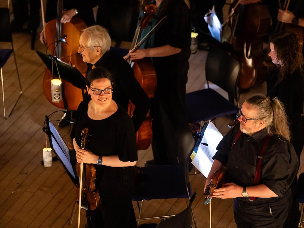 The orchestra stands. A violinist looks around with a smile.
