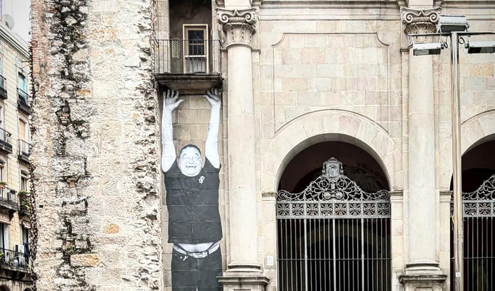 A photograph of a side of a stone building, with a graffiti image of a man lifting his arms up.