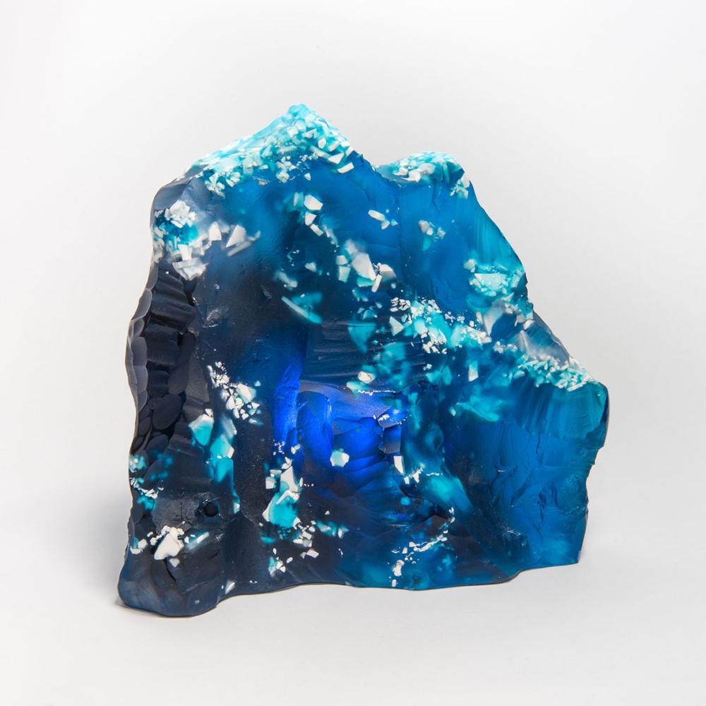 A glass sculpture by Jessamy Kelly. The sculpture is blue/turquoise glass and rock-like.
