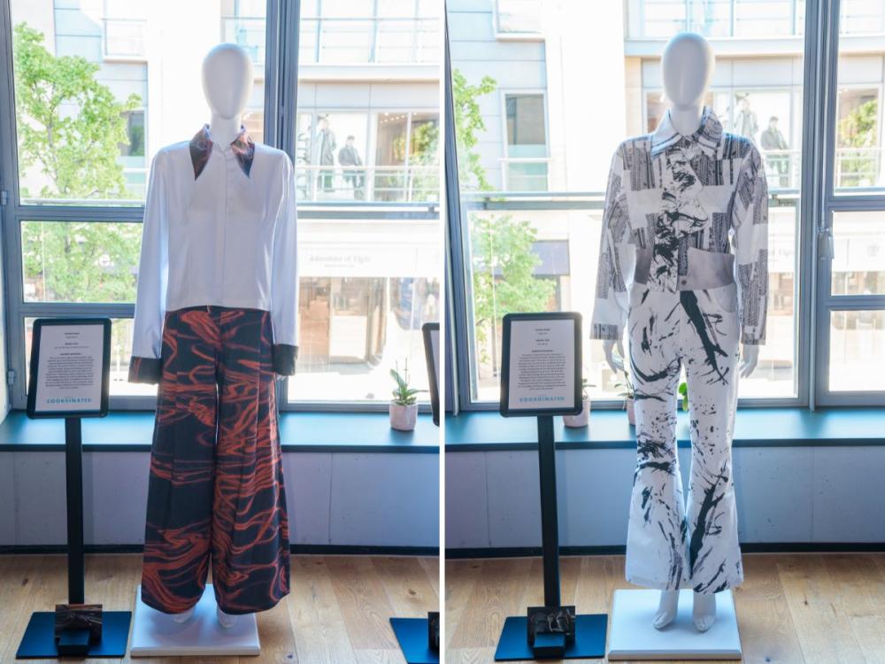 Two sets of garments on mannequins, each with trousers and a top. One has a terracotta and grey pattern on the trousers and collar, the rest of the shirt is white. The other has black and white pattern.