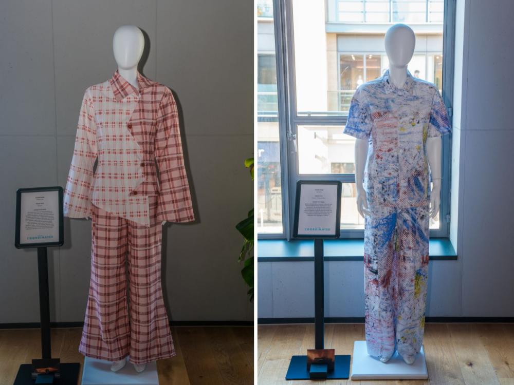 Two sets of garments on mannequins, each with trousers and a top. One is pink/red with contrasting check patterns and a zig zag front. The other is white, with a pattern in blue, black and yellow