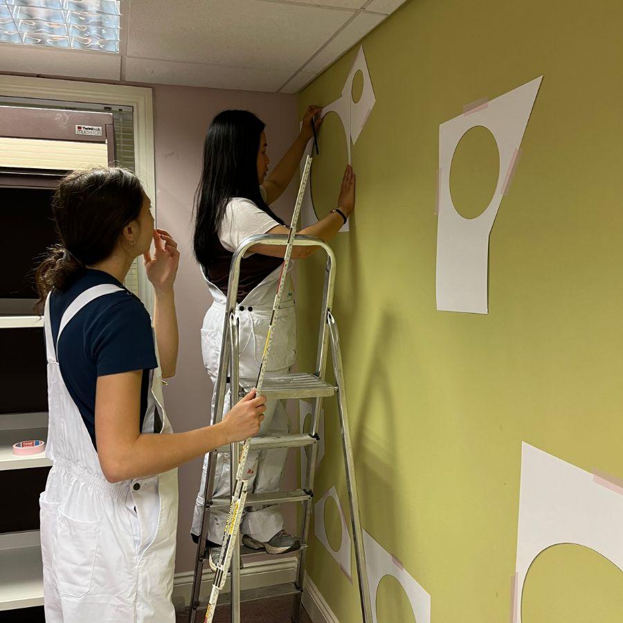 Two students are arranging paper templates of circles on a wall.
