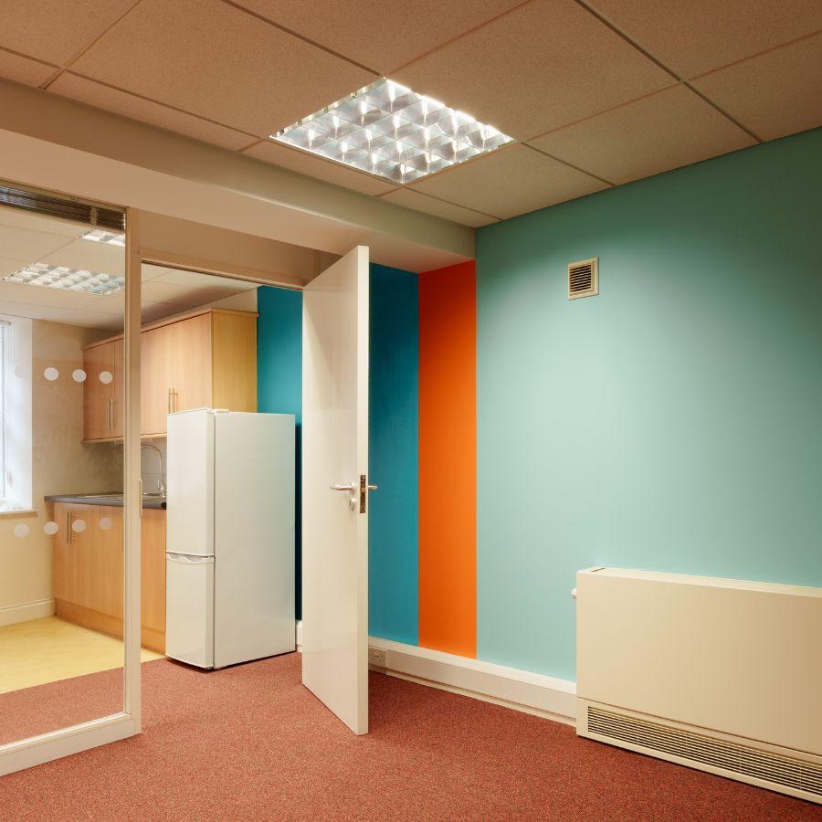 A door is open to a kitchen area. Behind the door is a brightly painted wall with vertical stripes.