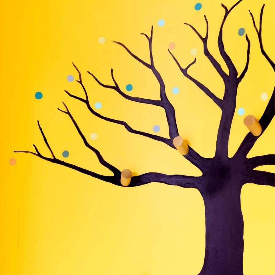 A close up of a painted tree. The branches are without leaves but brightly coloured circles float above some of them. You can see wooden pegs.