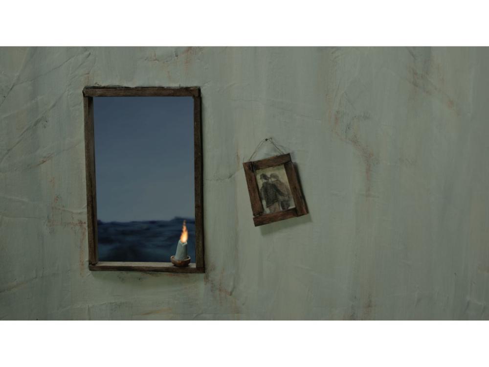 A rectangular window in a textured white wall shows a dark blue sea outside. There is a small candle on the window ledge. A small picture of two people side by side hangs from the wall.