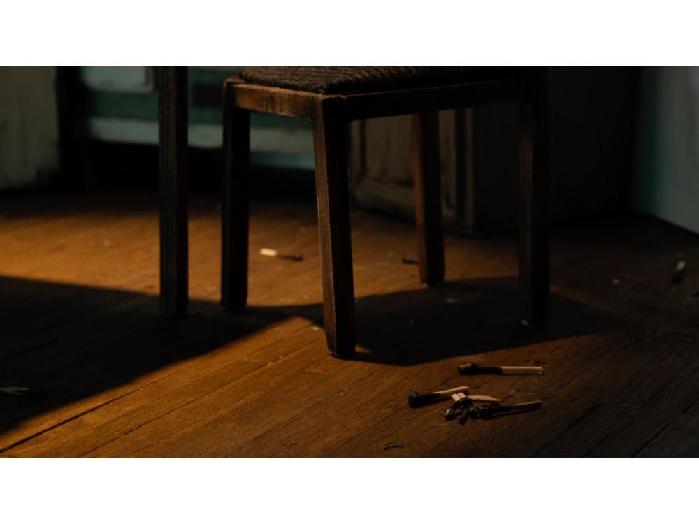 The legs of a chair on a wooden floor. A pile of spent matches lies on the floorboards.
