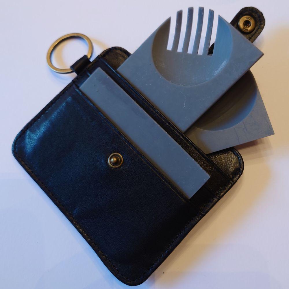 A wallet with several grey plastic cards emerging from it, each the shape of credit cards. The top, most visible one, has a circular bowl shape in the corner, and fork tines cut into it.