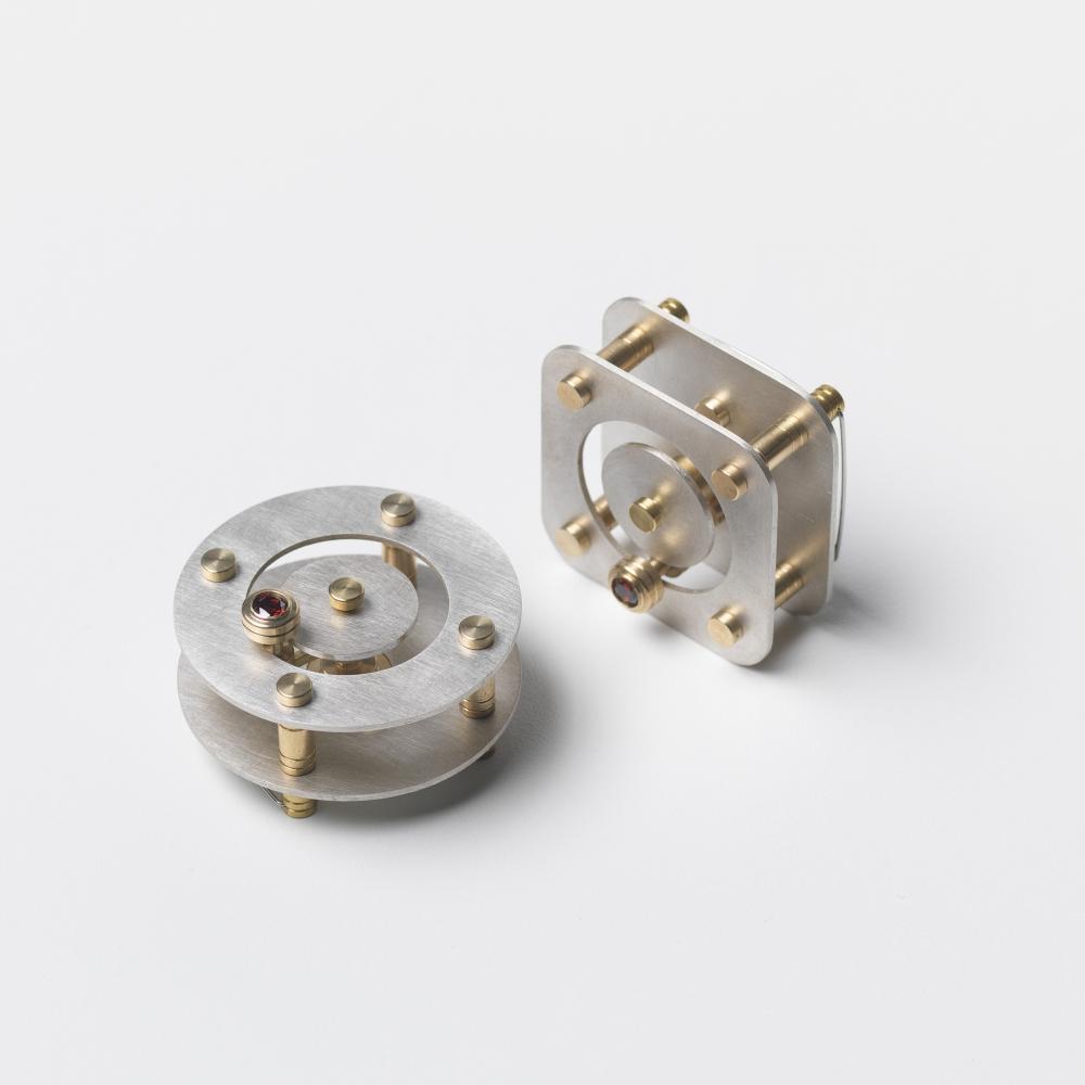 Two pieces of work, one circular, one square. each consists of flat, silver metal plates, connected by brass rods