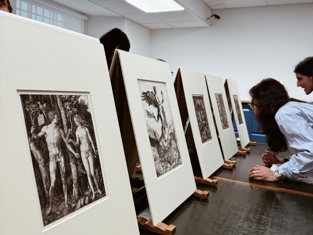 A student leans in to look at prints by Albrecht Durer on a table behind the scenes at a museum