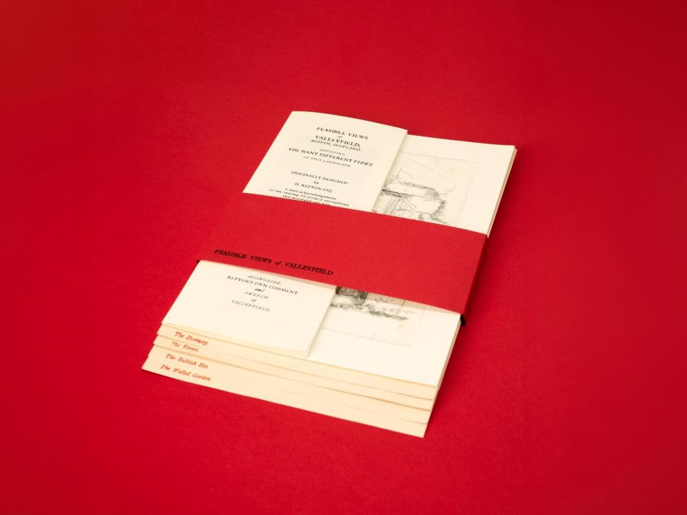 A set of cream booklets held together by a red paper band on a red background. The open top booklet is a mock-antique title page reading "Feasible Views of Valleyfield, Rosyth, Scotland", styled after landscape gardener Humphry Repton, with a faint pencil sketch on the facing page. Edge-printed tabs below read The Doorway, The Forest, The Rubbish Bin and The Walled Garden.
