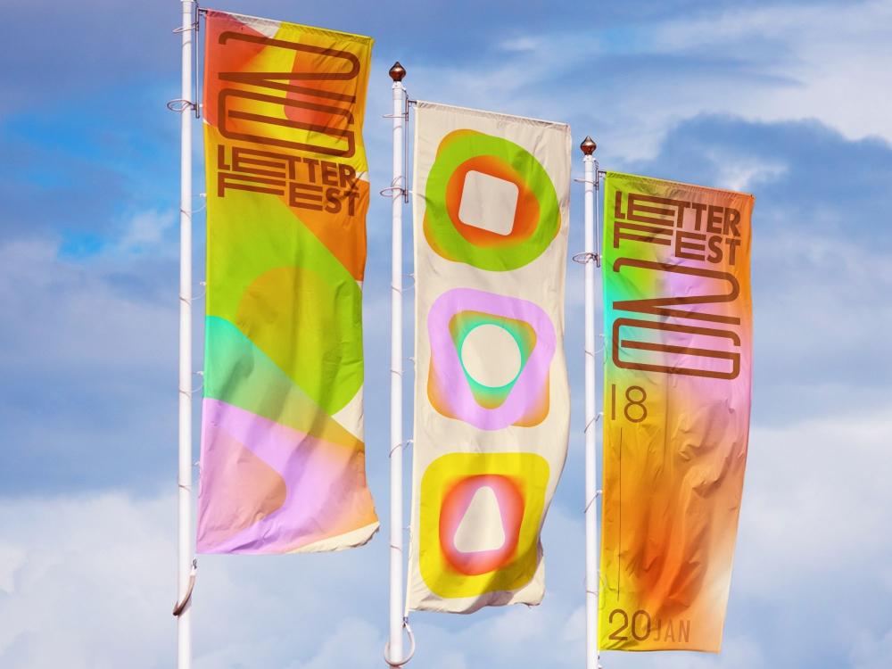 Three tall vertical banners on white flagpoles against a bright blue, partly cloudy sky. The outer two carry the "LetterFest 26" logotype in soft rainbow gradients of orange, green, pink and yellow, with the dates 18 to 20 January on the right-hand banner. The cream centre banner shows three rounded, glowing abstract shapes in the same gradient palette.